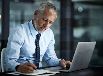 Business man sitting in front of laptop writing on papers