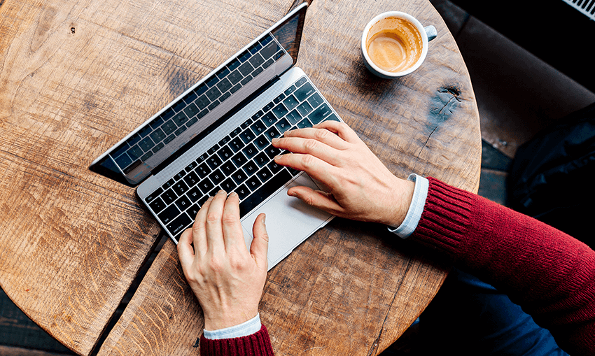 Person typing on computer with a cup of coffee near