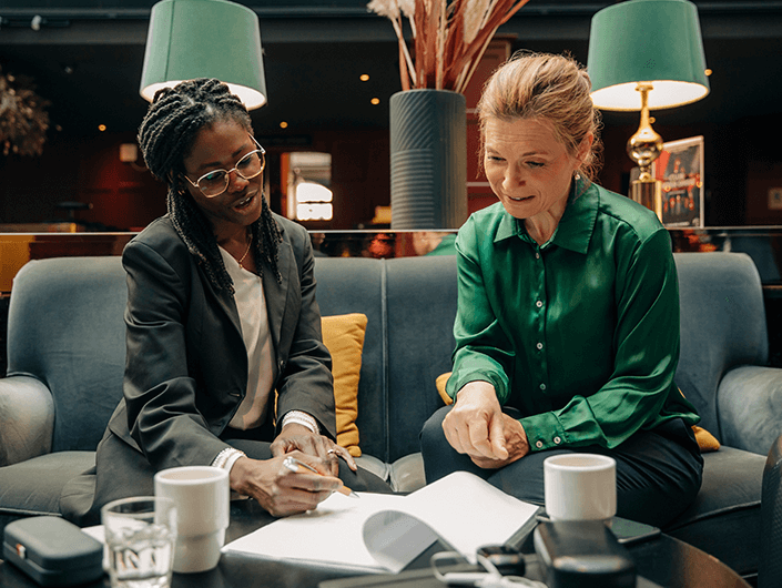 two diverse women meeting seated in dark room looking at papers