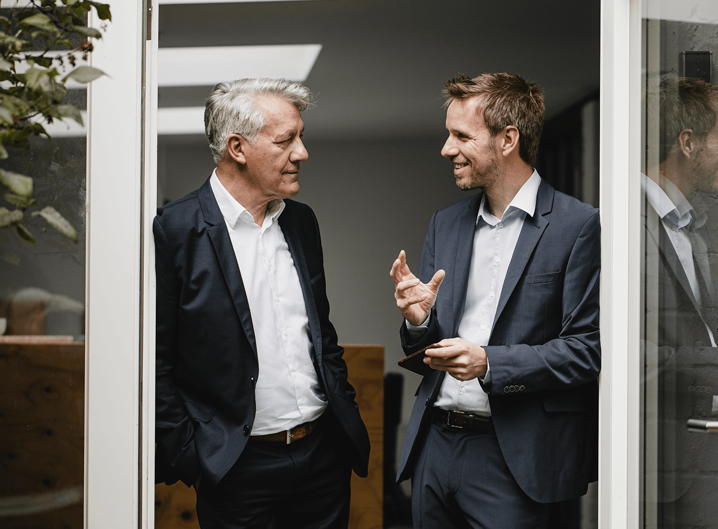 older and younger businessmen leaning against door jamb talking